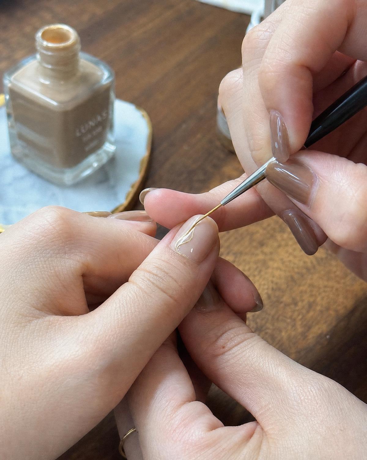 Nail technician painting a nude nail with a fine brush